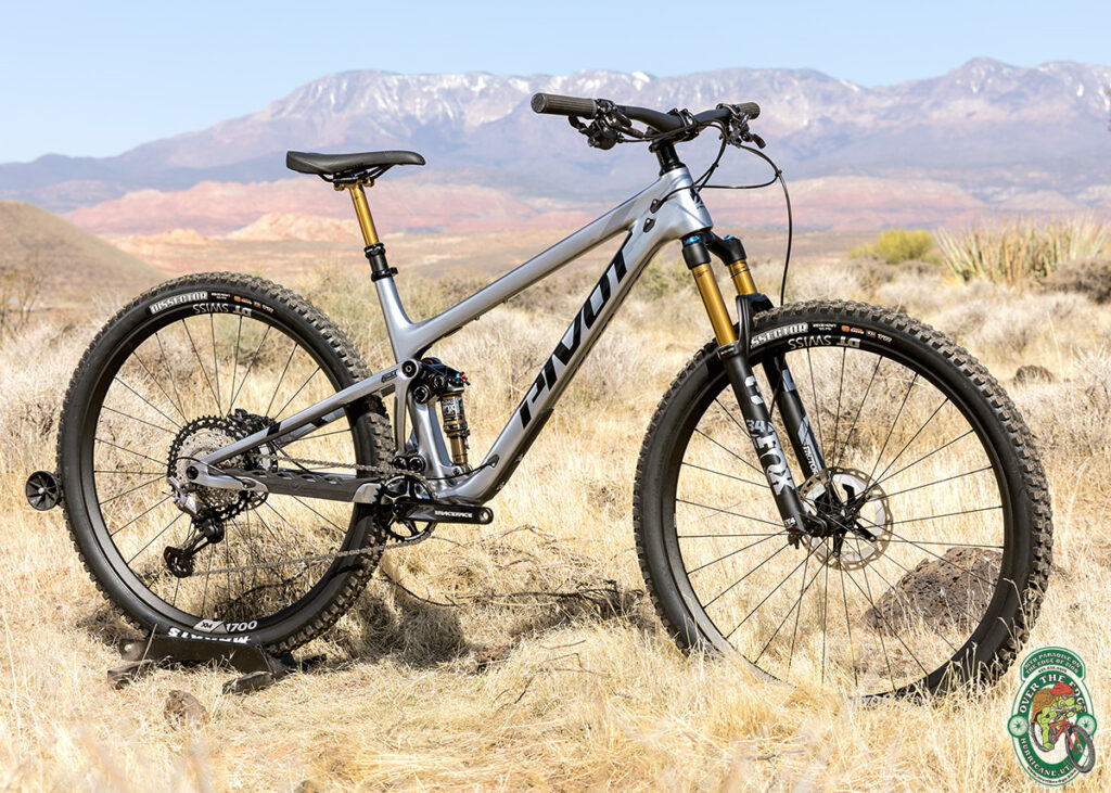 Silver Pivot full suspension mountain bike in desert with mountains in the background.