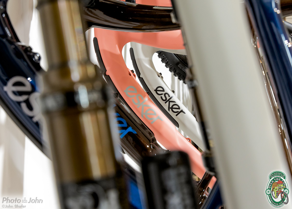 A closeup photo taken through the main triangle of hanging pink and gray carbon fiber mountain bike frames.