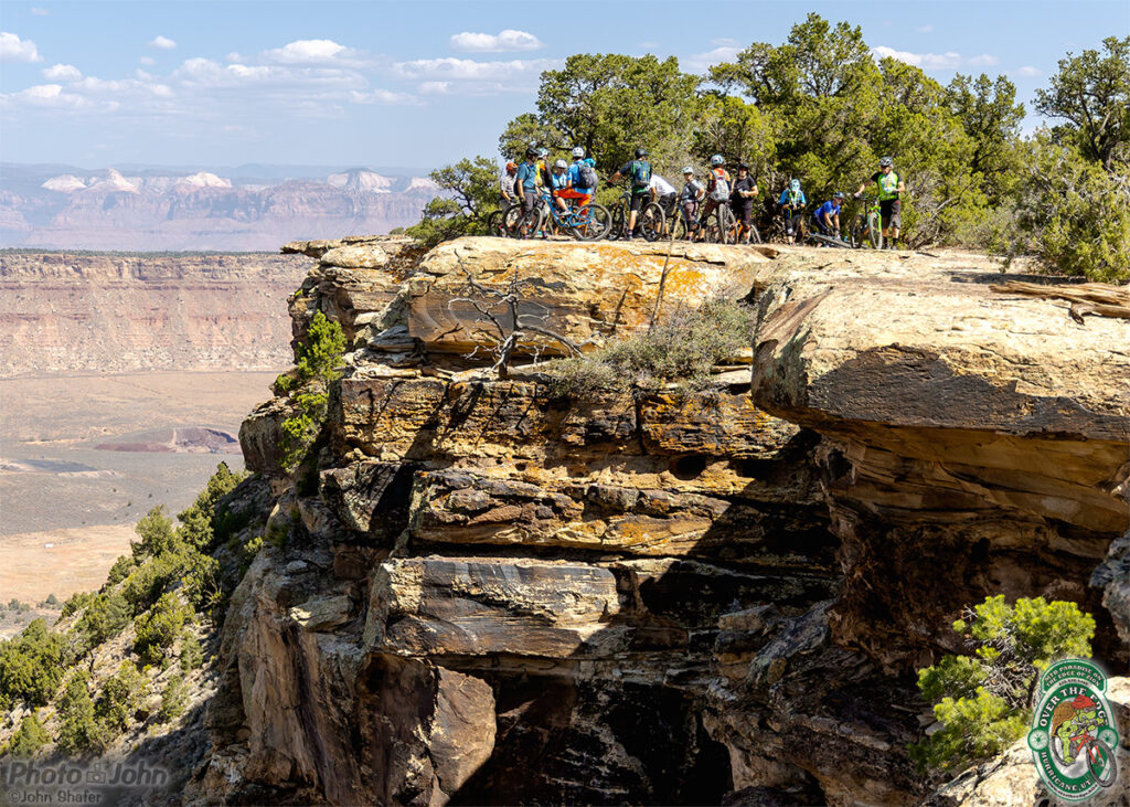 A group of mountain bikers hanging out on a the edge of a big cliff with Zion National Park in the background. 