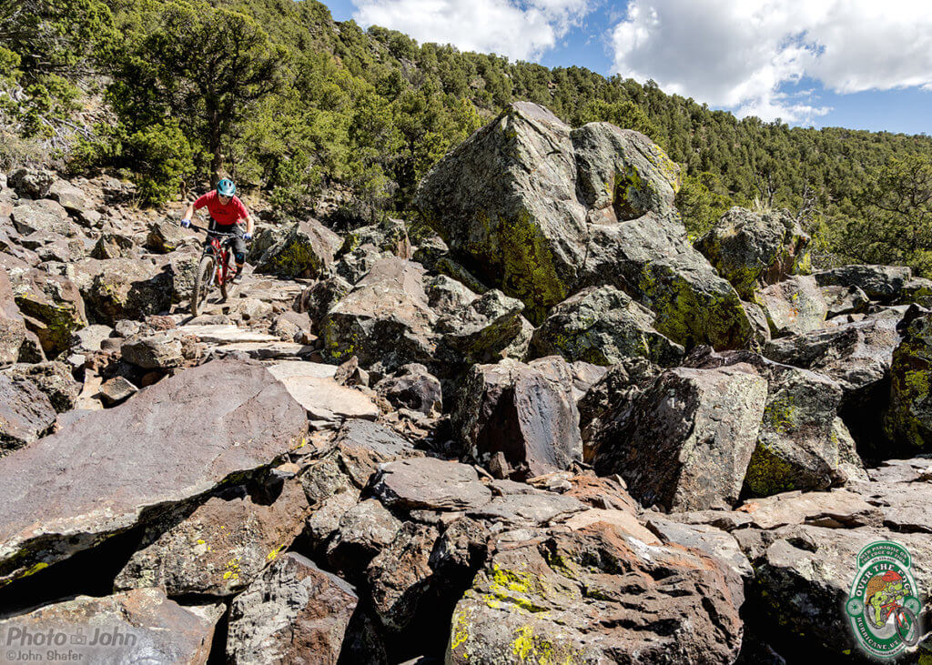 A wide-angle photo of a field of huge boulders with a small mountain biker riding through from the left. 
