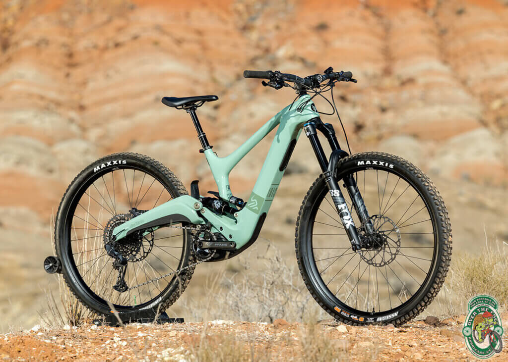An outdoor photo of a mint-green full-suspension mountain bike against a yellow-orange southwest hillside.