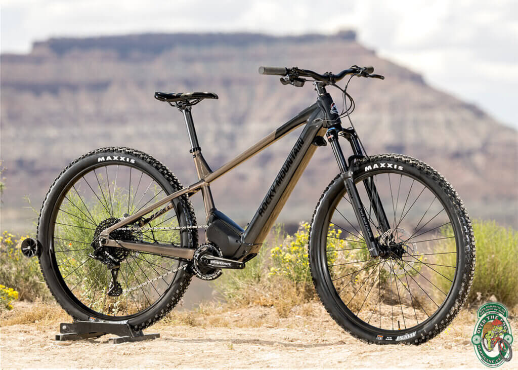 A photo of a two-tone, gold and black e-bike mountain bike against a Southern Utah desert butte background..