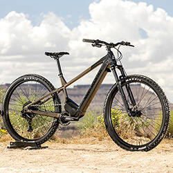 Thumbnail photo of a dark, two-tone mountain bike e-bike in a desert landscape with billowy clouds.