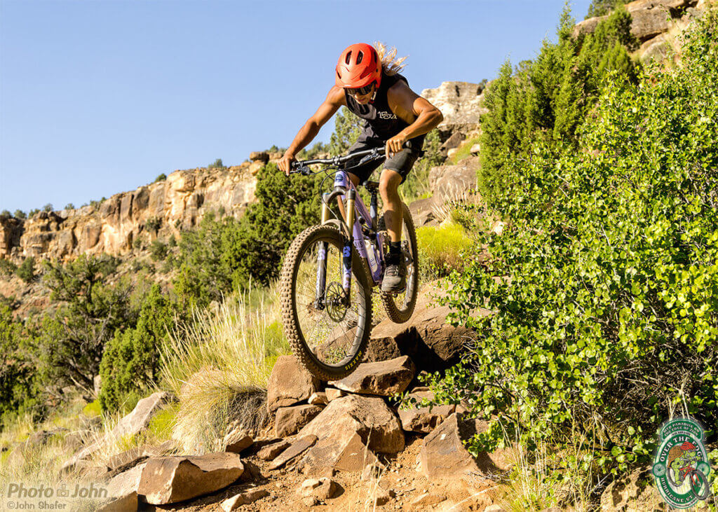 A mountain biker rides a steep, skinny trail that's mostly large, sharp sandstone rocks. 
