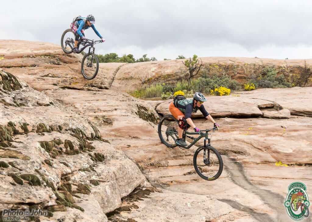 2023 Afterbike MTB gathering:  a photo of two women riding full-suspension mountain bikes down a steep, slickrock slope in Southern Utah. 